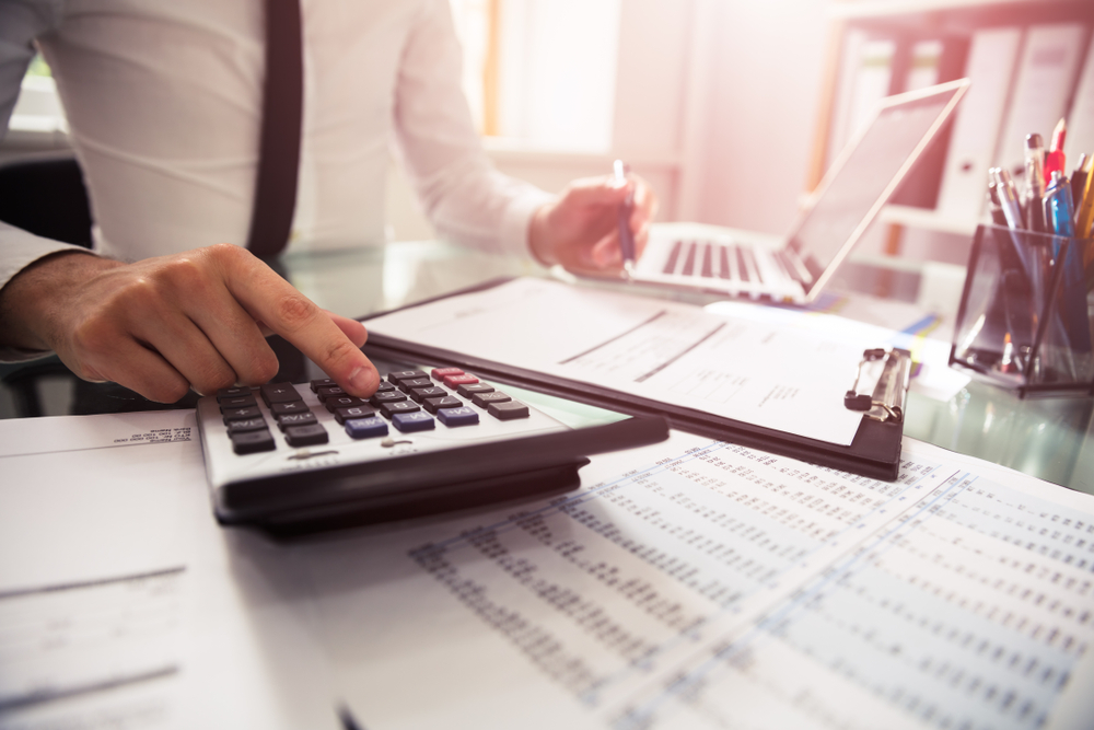 Businessman calculating financials on a desk with papers and a laptop, focused on managing expenses and budgets.