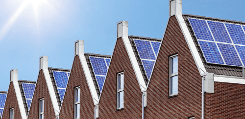 Solar panels are displayed on a row of houses under a blue sky.