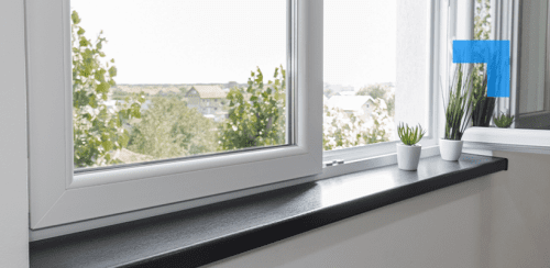 A modern white-framed window is partially open, revealing a view of suburban houses and trees outside. On the black windowsill inside, three small potted plants with spiky green leaves add a natural touch. A mirror on the right reflects the window and plants, enhancing the sense of space and light.