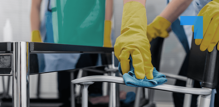 A person wearing yellow gloves cleaning a chair with a blue cloth.