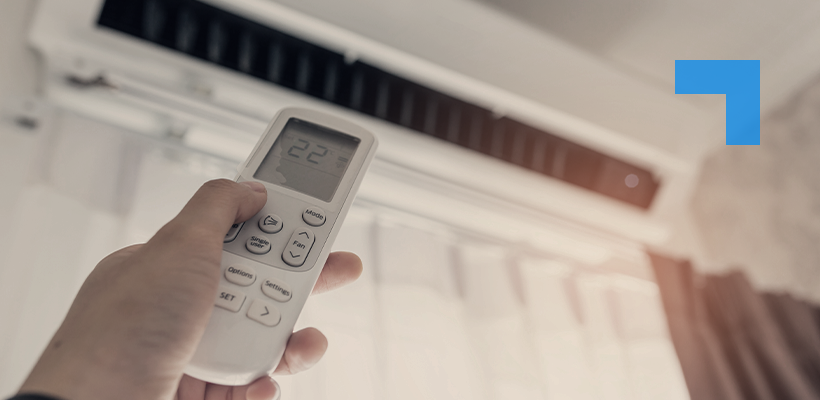 A person holding a remote control pointed at a wall-mounted air conditioner, with the display showing 22°C.