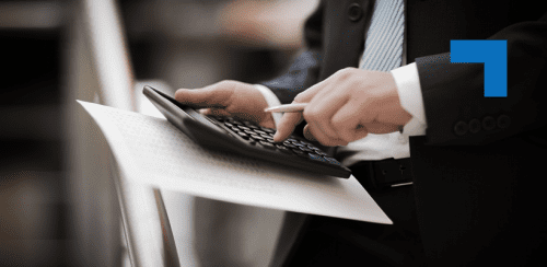 A businessman in a suit holding documents and using a calculator, possibly reviewing financial data or performing calculations.
