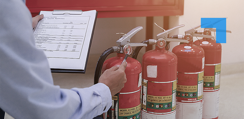 Fire safety technician carrying out inspection of multiple fire extinguishers with checklist on clipboard.