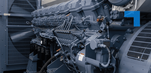 Close-up of a large industrial generator engine with visible fuel lines, pipes, and mechanical components inside a power generation facility.