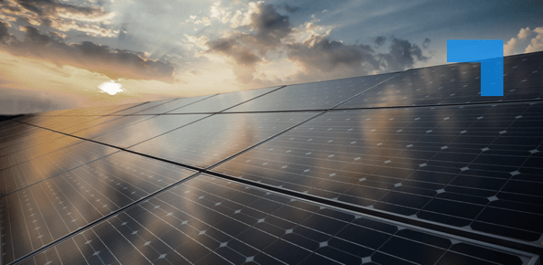 Solar panels arranged in rows under a partly cloudy sky at sunset, reflecting sunlight, with warm orange and blue tones across the scene.