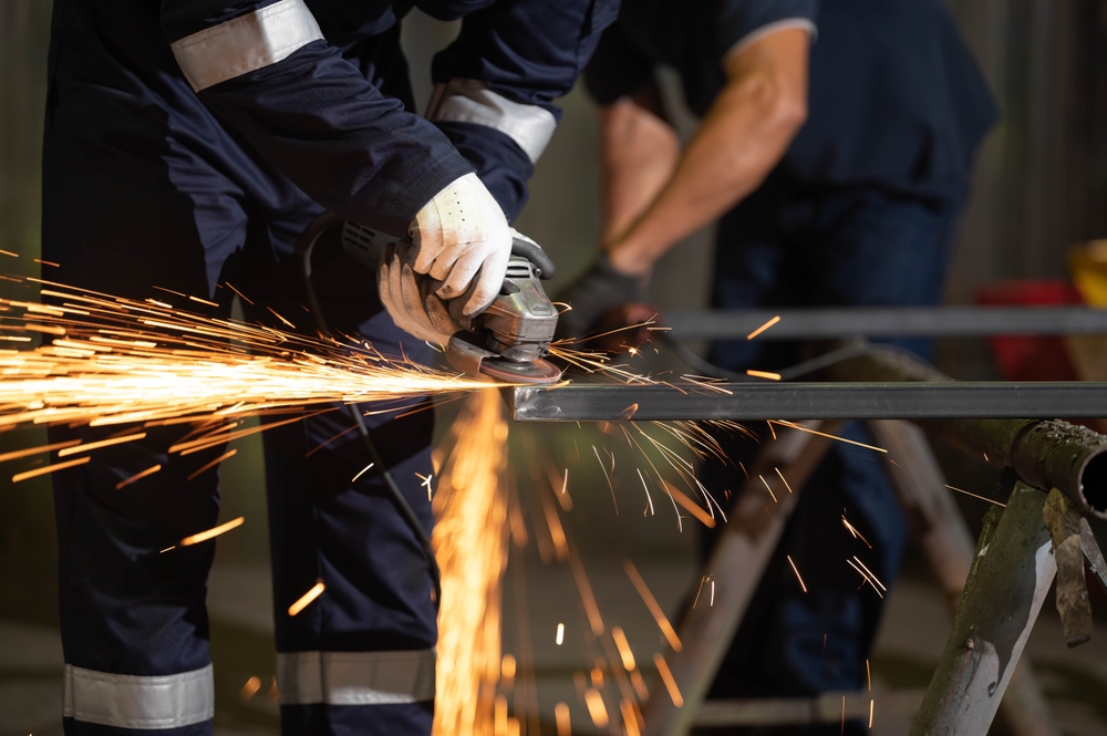 Engineering technician using an angle grinder to fabricate metal components in a manufacturing workshop
