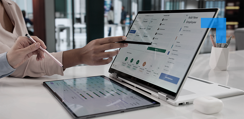 A professional using a tablet and touchscreen laptop displaying HR and workforce management software dashboard in a modern office setting.