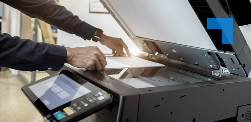 A person loads documents into a high-capacity office scanner or multifunction printer, illustrating document digitisation and records management services in a professional workplace setting.