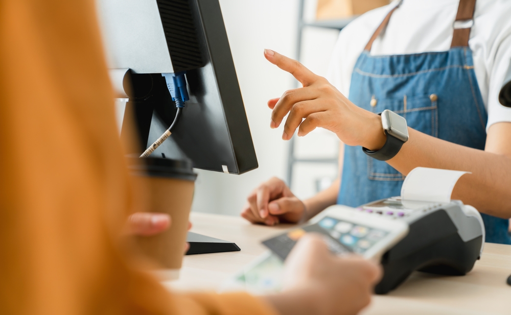 Retail employee assisting a customer at a point-of-sale checkout terminal