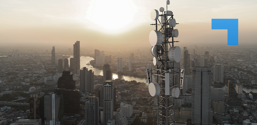 A telecommunications mast fitted with multiple microwave dishes and antennas overlooking a large city skyline at sunset, representing secure radio communications and critical network infrastructure.