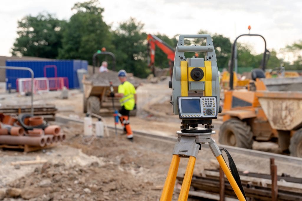 Building surveying equipment on a construction site with a construction worker in a high vis jacket in the background