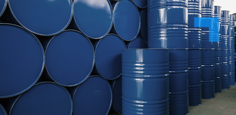 Rows of stacked blue industrial steel drums and barrels in a warehouse, with circular barrel ends visible on the left and upright drums extending into the background on the right.