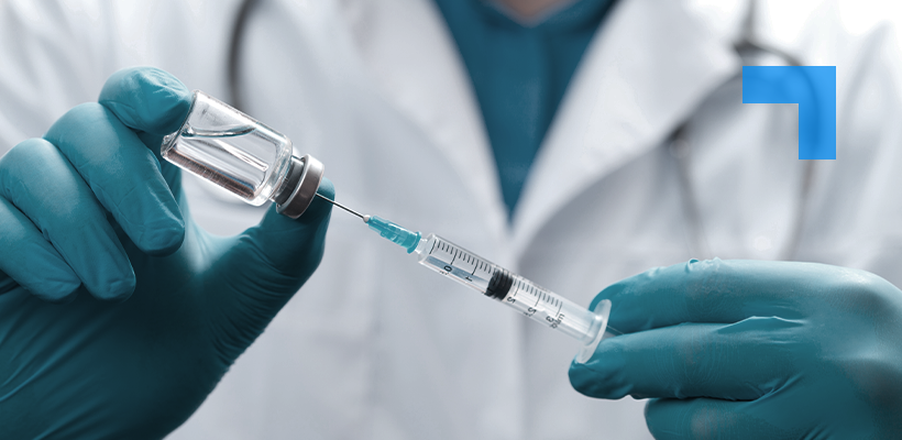 A medical professional wearing blue gloves draws liquid from a vial into a syringe.