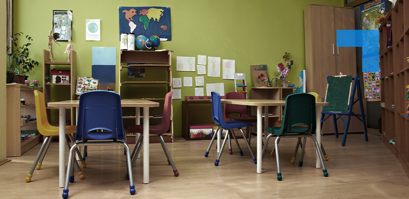 A brightly coloured primary school classroom with wooden desks, multi-coloured chairs and educational displays on green walls.